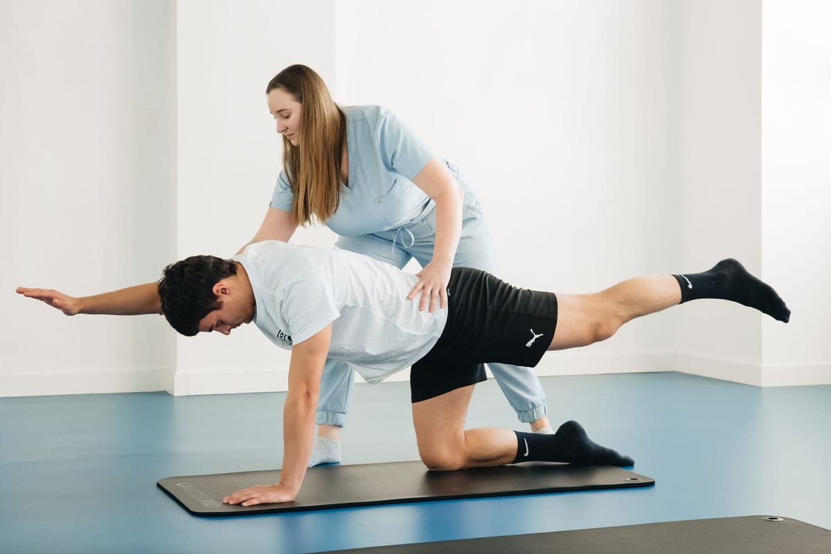 A physiotherapist guiding a patient through a stabilization exercise on a mat